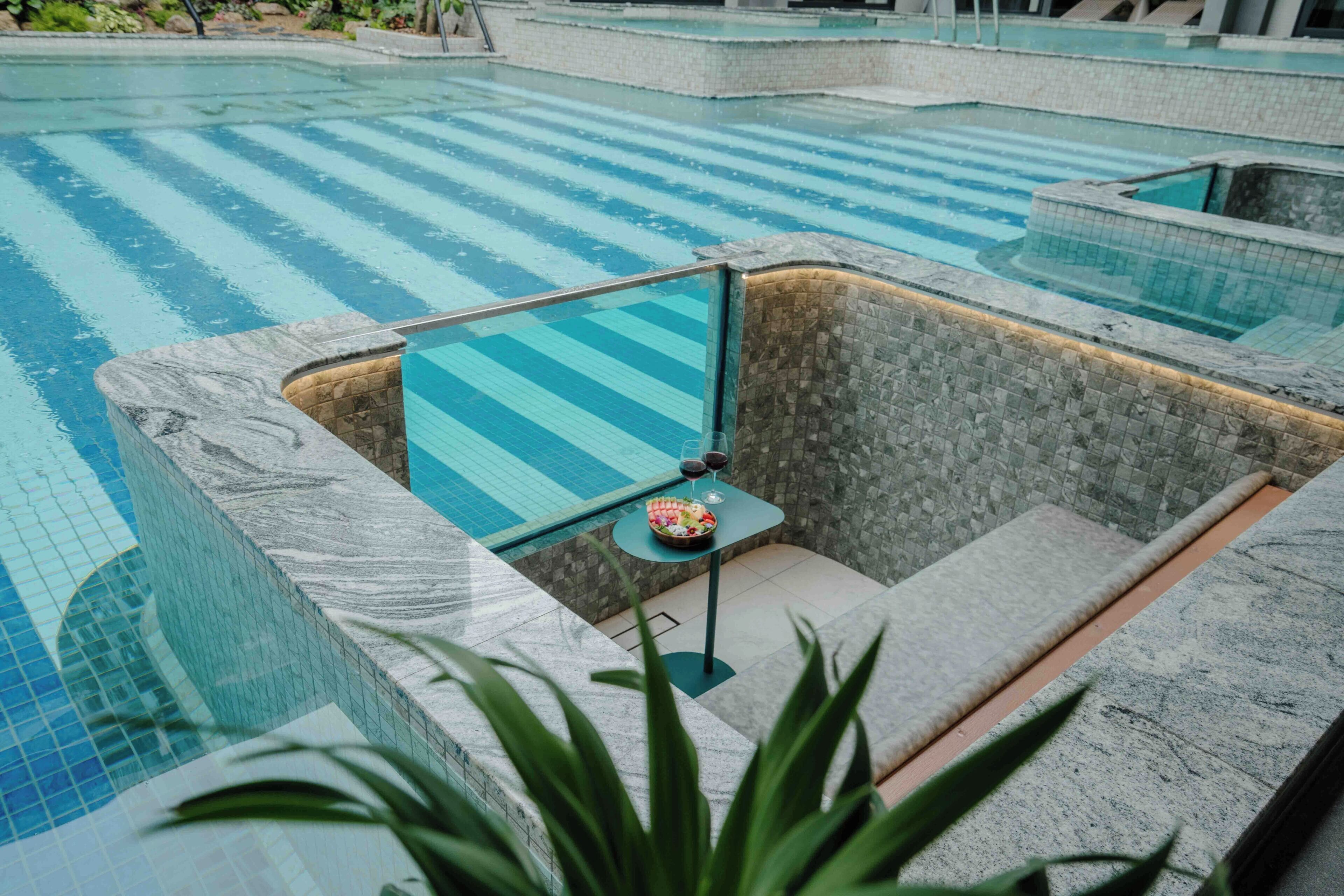 Ein Schwimmbecken mit Fliesen umrandet und einem kleinen Sitzbereich mit Tisch und Stühlen.