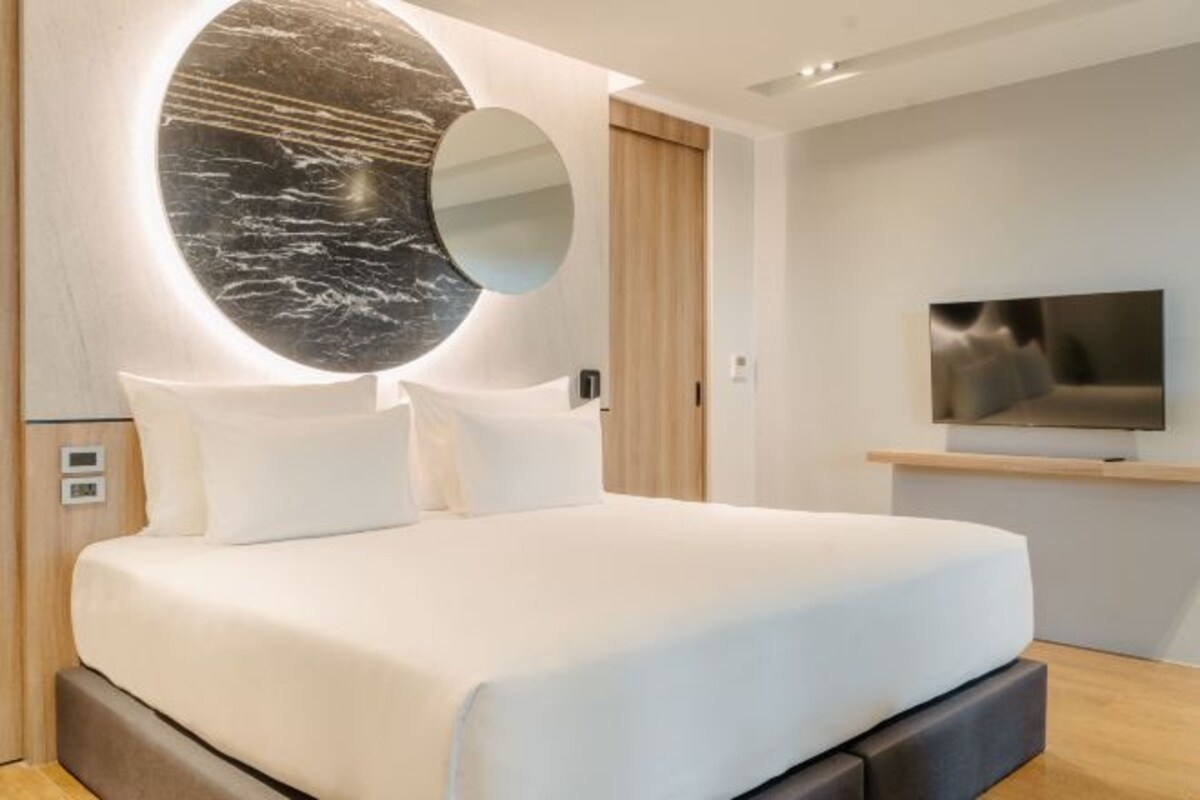 A modern bedroom with a large bed, a round mirror, a flat-screen TV, and a wooden door.