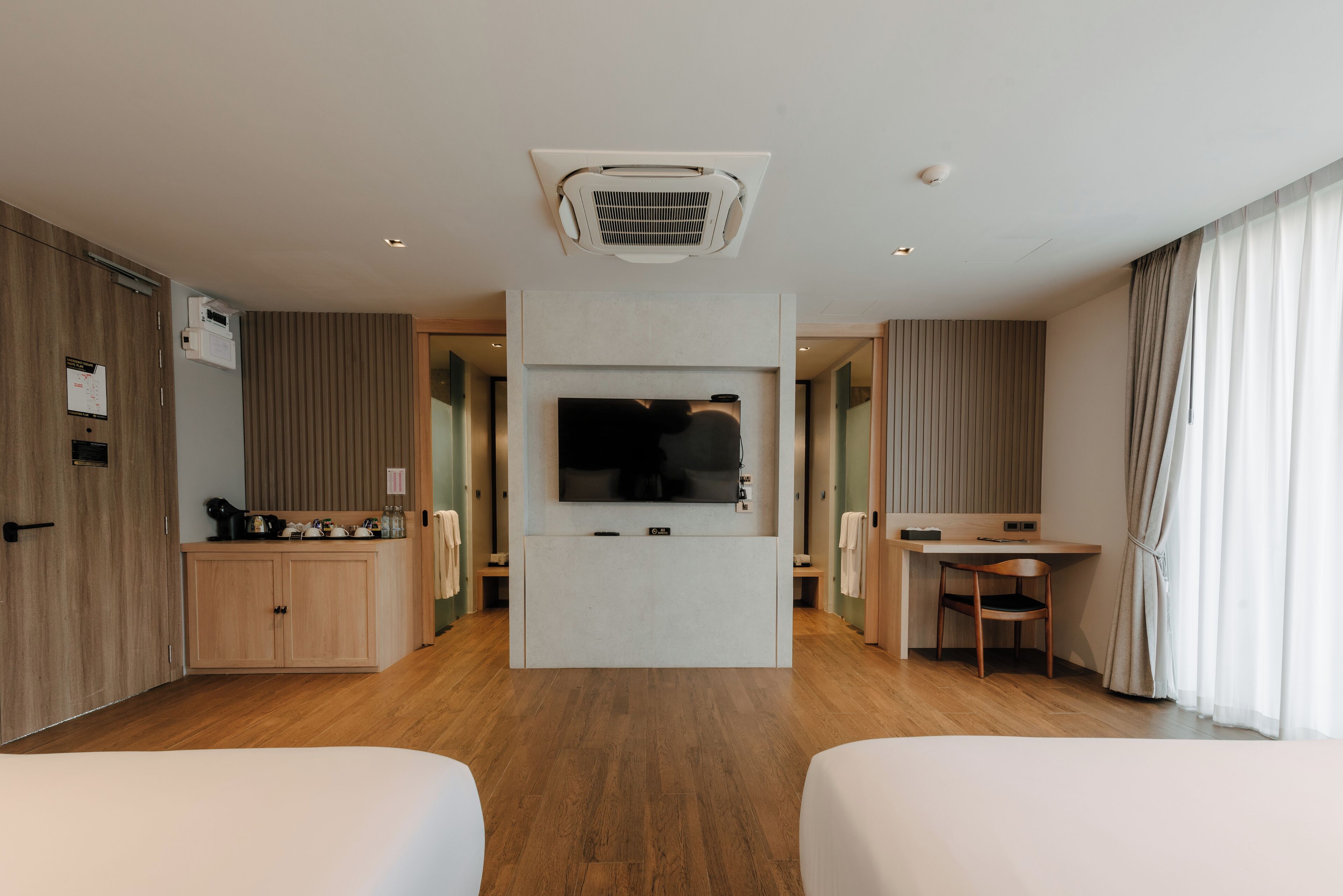 A hotel room with a flat-screen TV, wooden flooring, a desk with a chair, and a wardrobe.