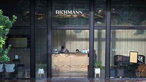 A reception desk with the name "RICHMANN" above it, two people behind the desk, and potted plants on either side.