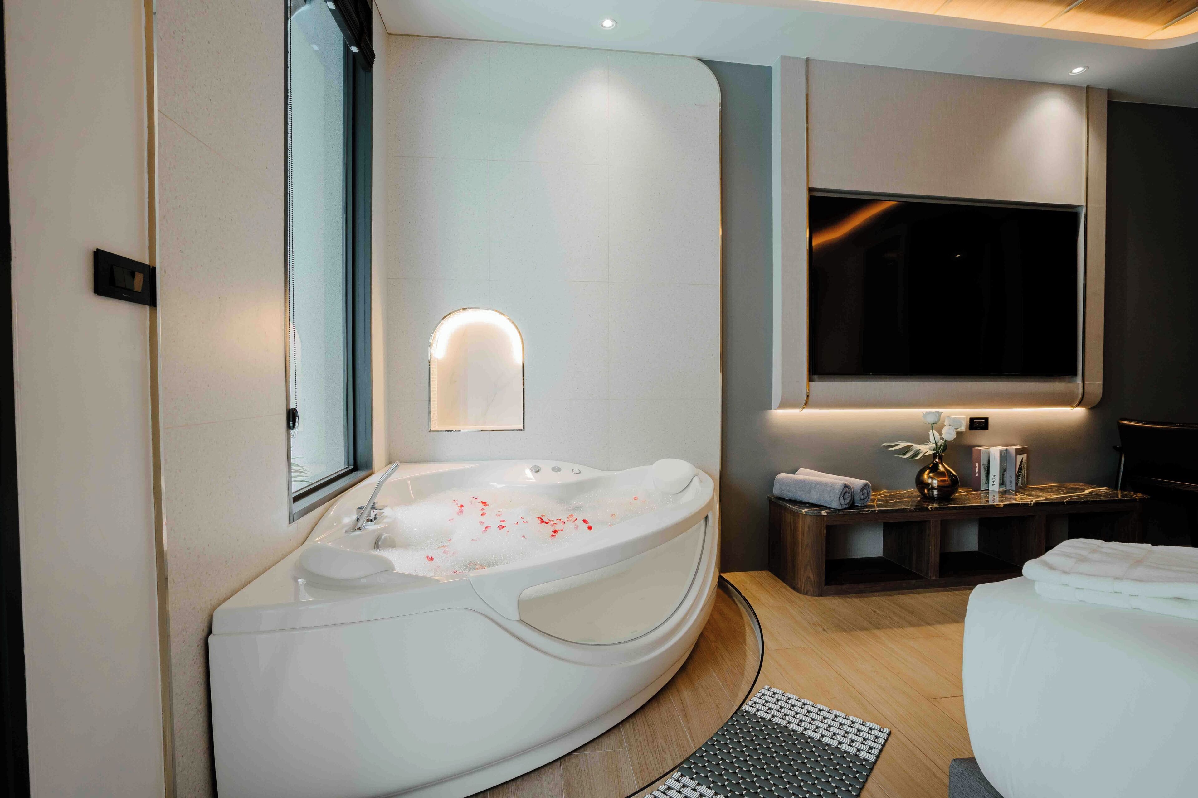 A modern bathroom with a large bathtub, a vanity with a mirror, and a television mounted on the wall.