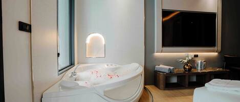 A modern bathroom with a large bathtub, a vanity with a mirror, and a television mounted on the wall.