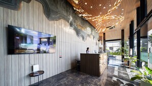 A modern reception area with a wooden reception desk, a mounted television, and a ceiling with a unique light fixture. - RICHMANN RESORT HOTEL HATYAI (Hat Yai)