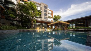 A modern hotel with a clear pool, outdoor seating, and lush greenery.