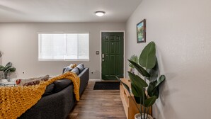 Un salon avec un canapé, une couverture jaune, une porte verte et une plante en pot.