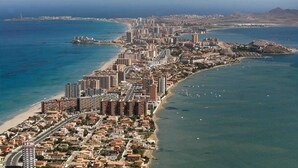Vista aérea de uma cidade costeira com área urbana densa, uma praia e um porto de iates.