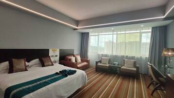 Quarto de hotel com uma cama grande, duas áreas de estar, uma escrivaninha e uma janela com cortinas.