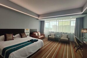 A hotel room with a large bed, two seating areas, a desk, and a window with curtains.