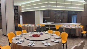 Une salle de conférence dotée de plusieurs tables, chacune étant mise avec des assiettes, des couverts et des bols. La salle présente un design moderne, avec une table centrale blanche et des chaises jaunes disposées autour.