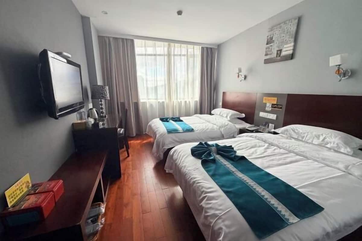 A hotel room with two beds, a TV, a desk, and a window with curtains.