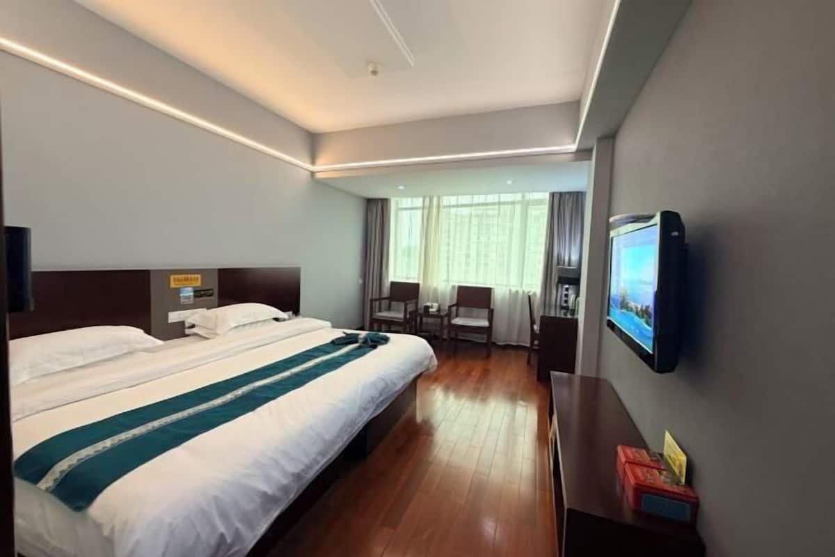 A hotel room with a large bed, a desk, a chair, a TV, and a window with curtains.