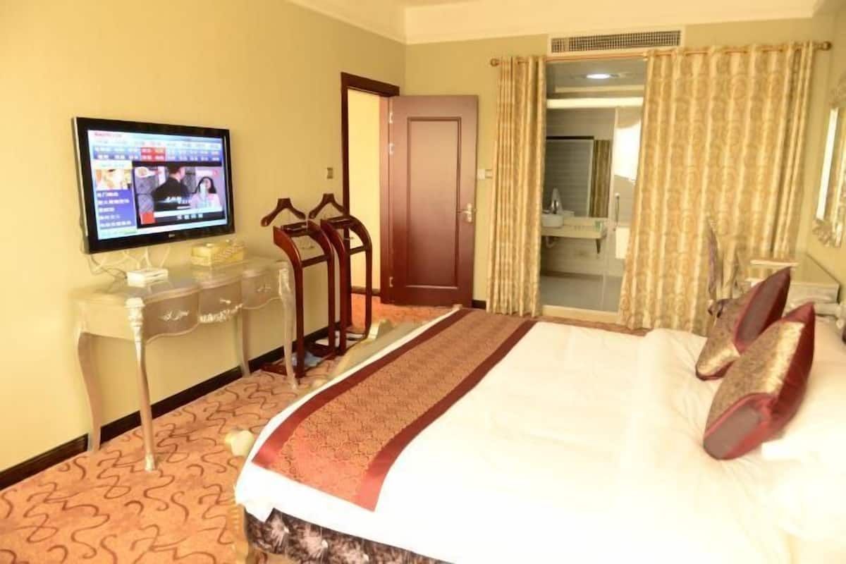 A hotel room with a bed, a television on a stand, a desk with a chair, and a door leading to a bathroom.