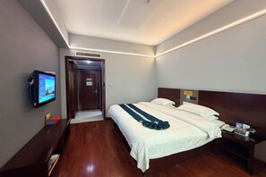 A hotel room with a bed, bedside table, TV, and a door leading to another room.