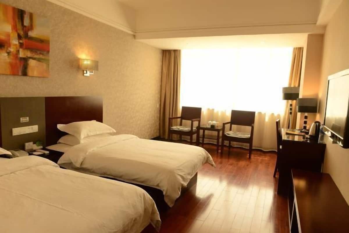 A hotel room with two beds, a desk, a chair, and a television.