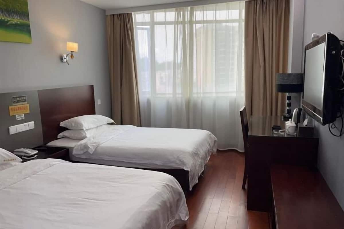 A hotel room with two single beds, a wooden desk with a mirror, a television, and a window with curtains.