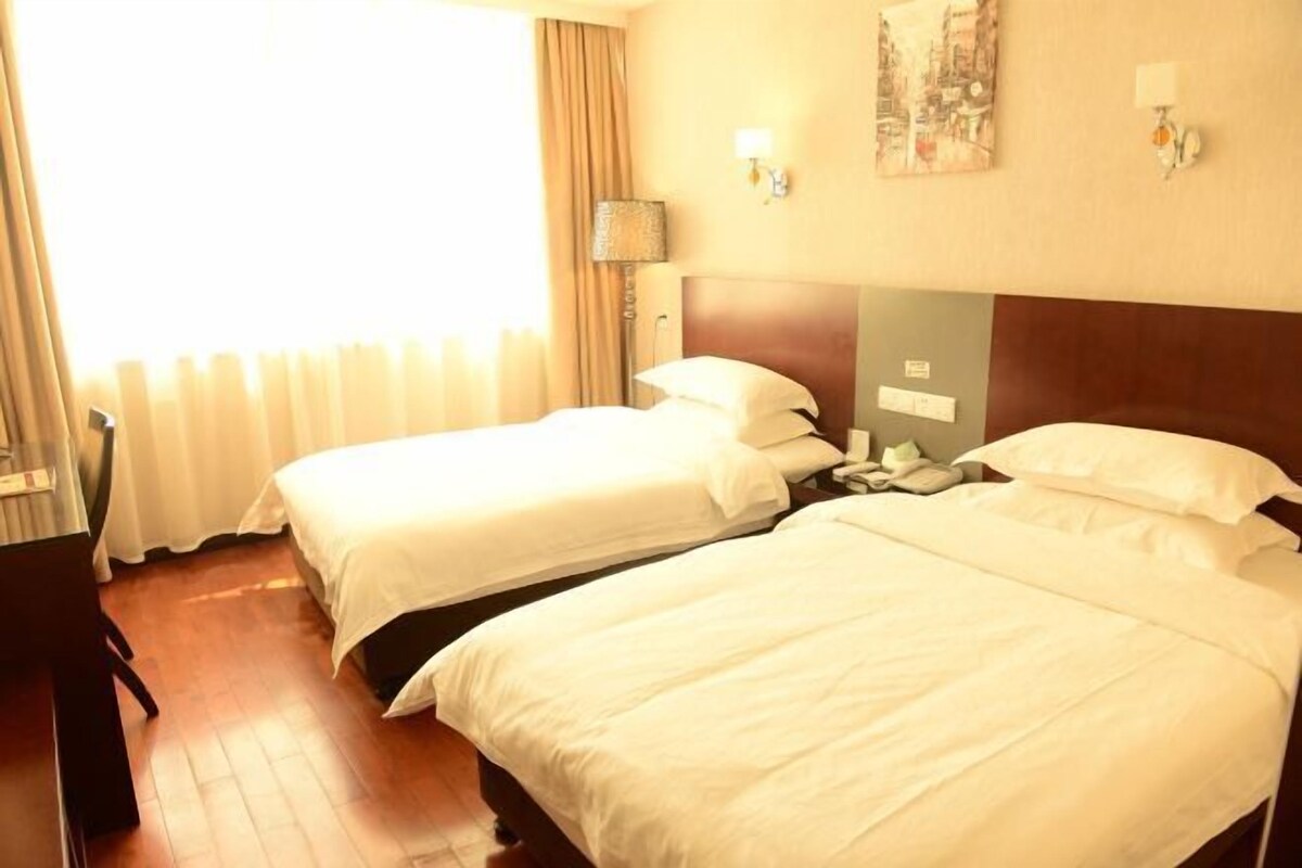 A hotel room with two beds, a desk, a lamp, and a window with curtains.