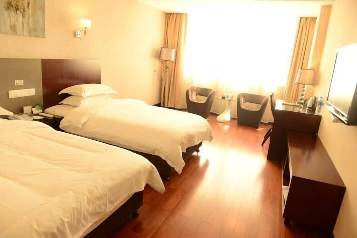A hotel room with two beds, a desk, a chair, and a TV.