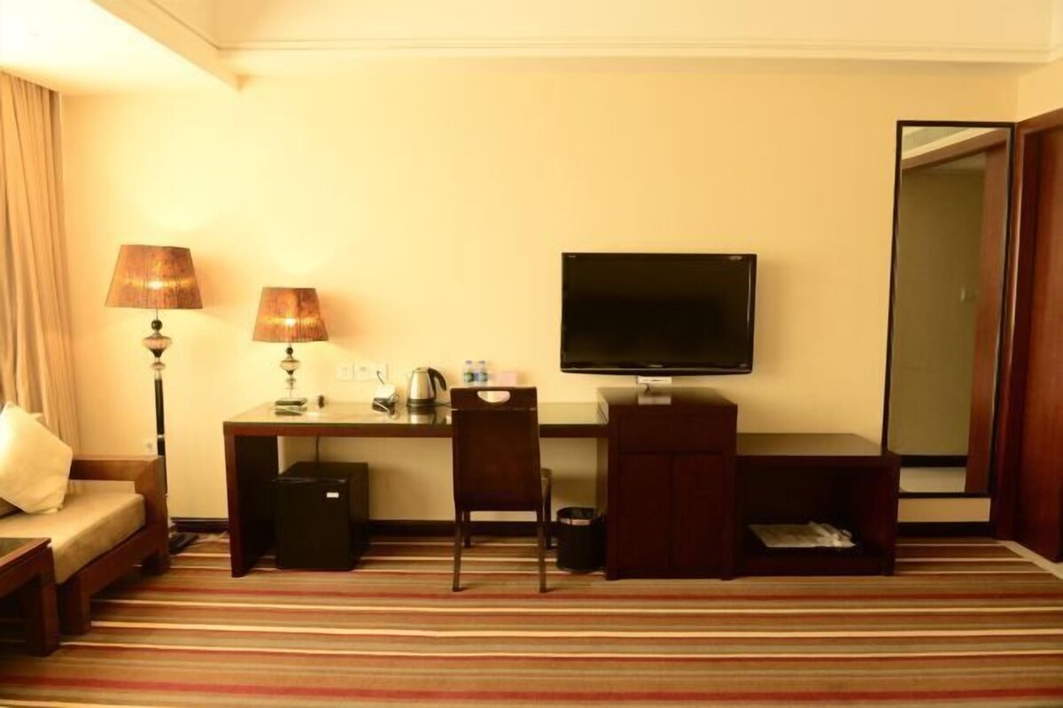 A hotel room with a bed, a desk with a chair, a television, and a small cabinet.