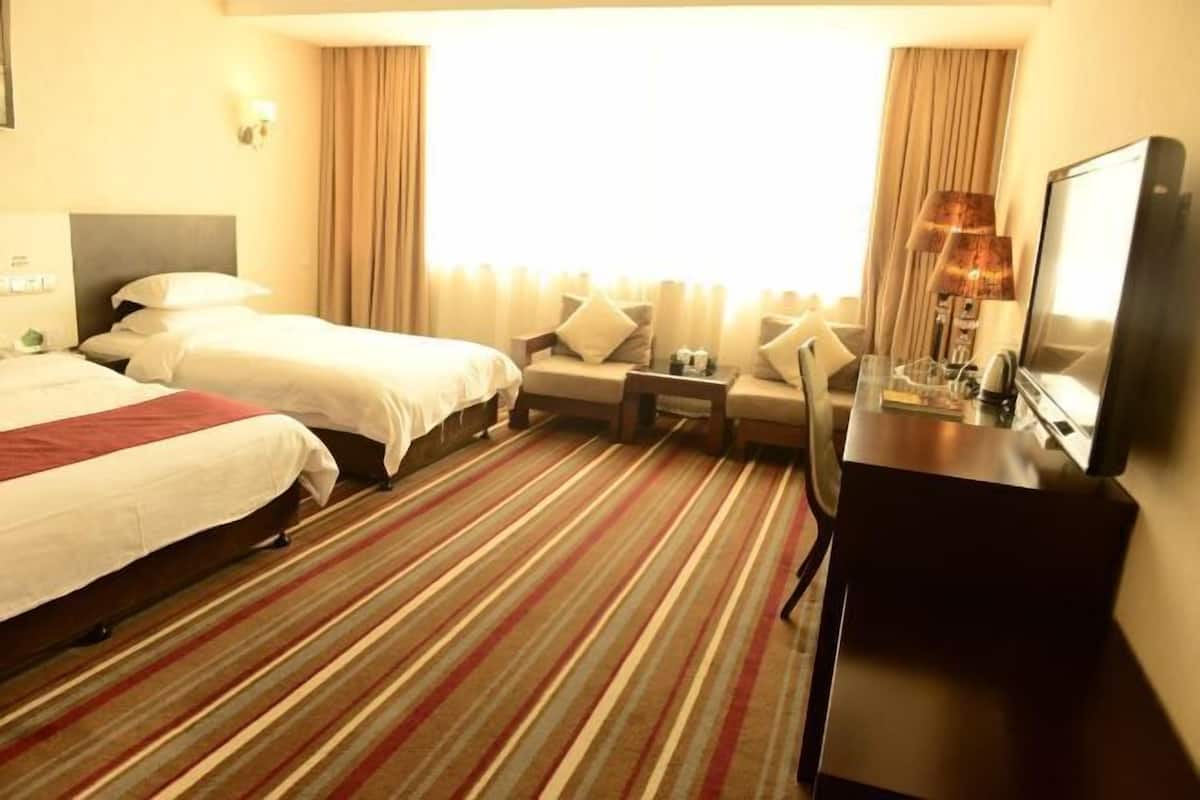A hotel room with two beds, a desk, a chair, a TV, and a window with curtains.