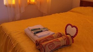 A room with a bed, a window with curtains, a bedside table with a heart-shaped mirror, and a towel. - Live N Love (Pasuquin)