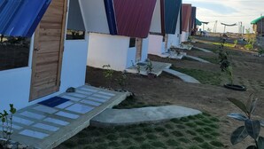 A row of small, single-story cabins with sloped roofs, arranged in a linear fashion along a dirt path. Each cabin has a small porch area with steps leading up to the entrance. - Live N Love (Pasuquin)
