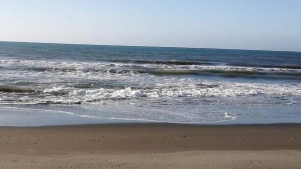 A sandy beach with visible footprints and waves approaching the shore. - Live N Love (Pasuquin)
