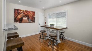 Une cuisine avec un plan de travail en bois, des tabourets de bar, un tableau représentant un pont et une fenêtre avec des stores.