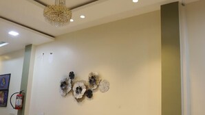 A hallway with a chandelier, recessed ceiling lights, and wall-mounted decorative flowers. - Hotel Virasat Palace By GRB (Mathura)