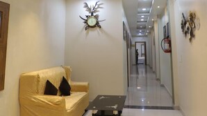 A hallway with a sofa and a coffee table, a chandelier, recessed lighting, and a clock on the wall. - Hotel Virasat Palace By GRB (Mathura)