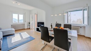 A modern living room with a sofa, dining table, chairs, and a TV. - Ca Gina Panoramica in Lugano (Lugano)