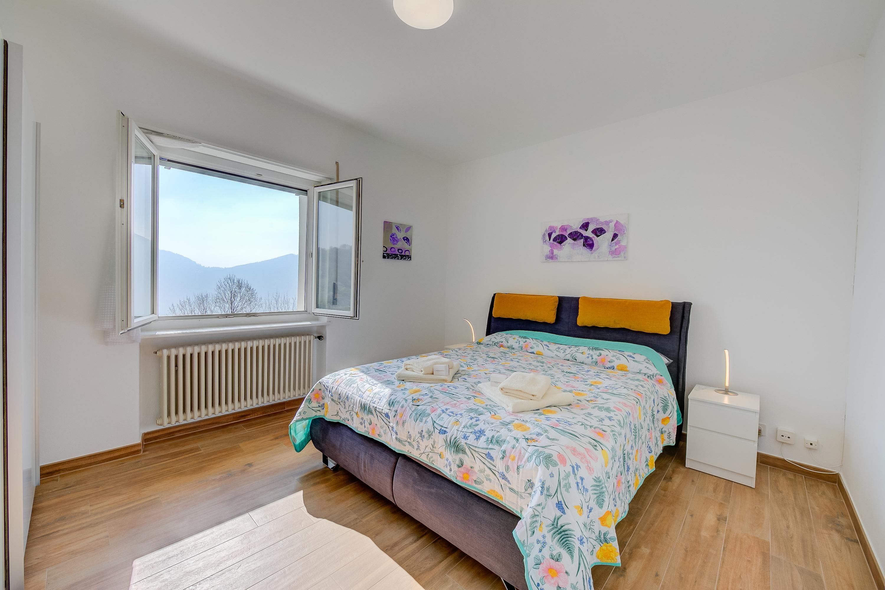 Un dormitorio con cama, mesita de noche, ventana y radiador.