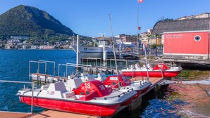 Un port de plaisance où sont amarrés plusieurs bateaux rouges et blancs, un bâtiment rouge avec une enseigne, et un paysage montagneux en arrière-plan.