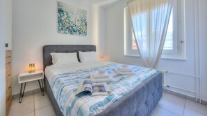 Une chambre moderne avec un grand lit, une table de chevet avec une lampe, un tableau au mur et une fenêtre avec des rideaux.