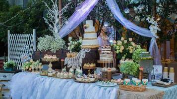 Una mesa de postres con diversos pasteles y repostería, rodeada de telas decorativas y arreglos florales.
