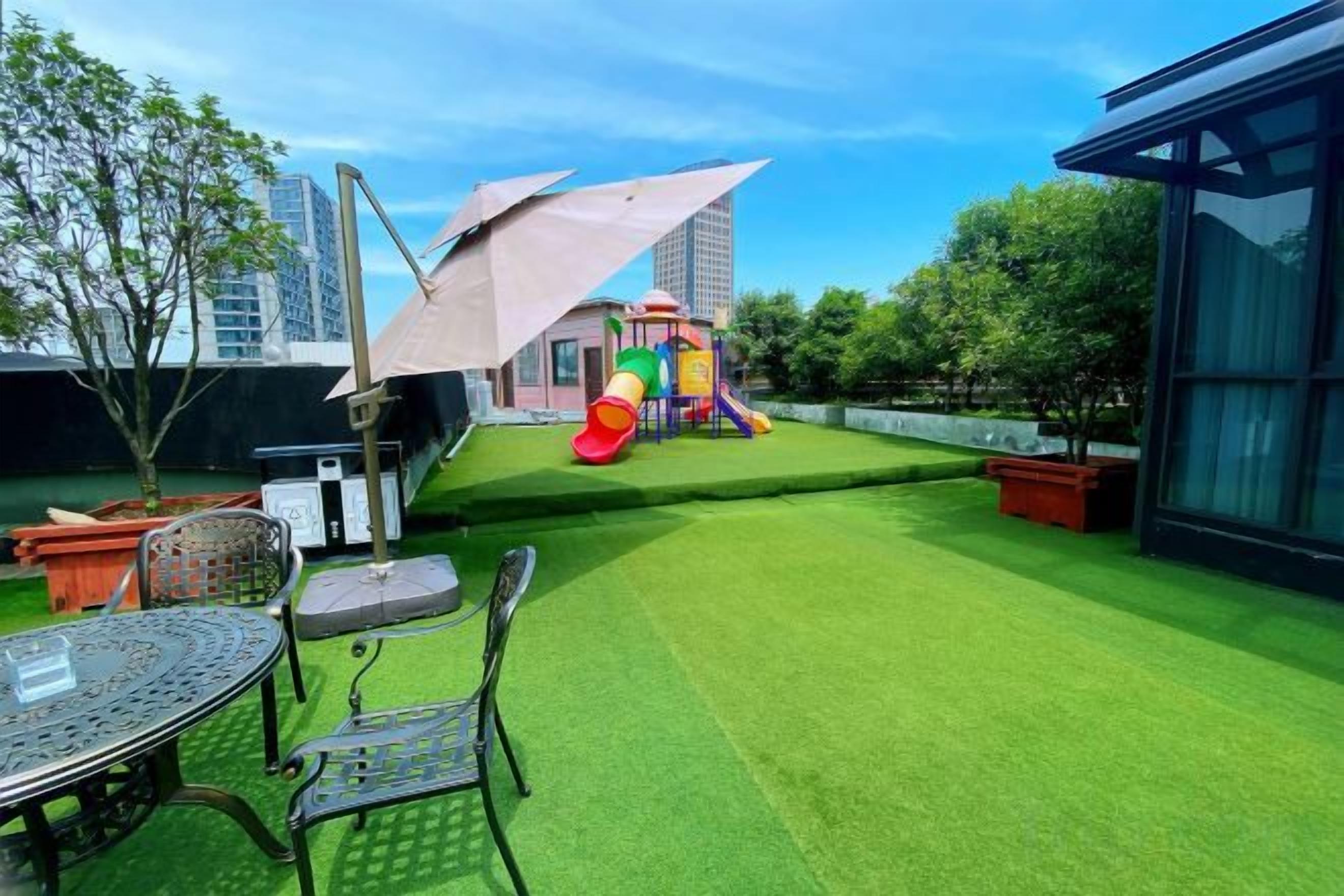A rooftop garden with artificial grass, a children's play area, and a table with chairs.