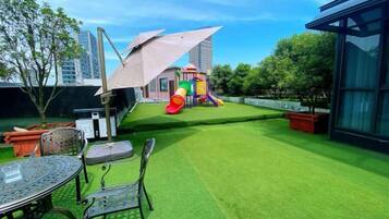 A rooftop garden with artificial grass, a children's play area, and a table with chairs.