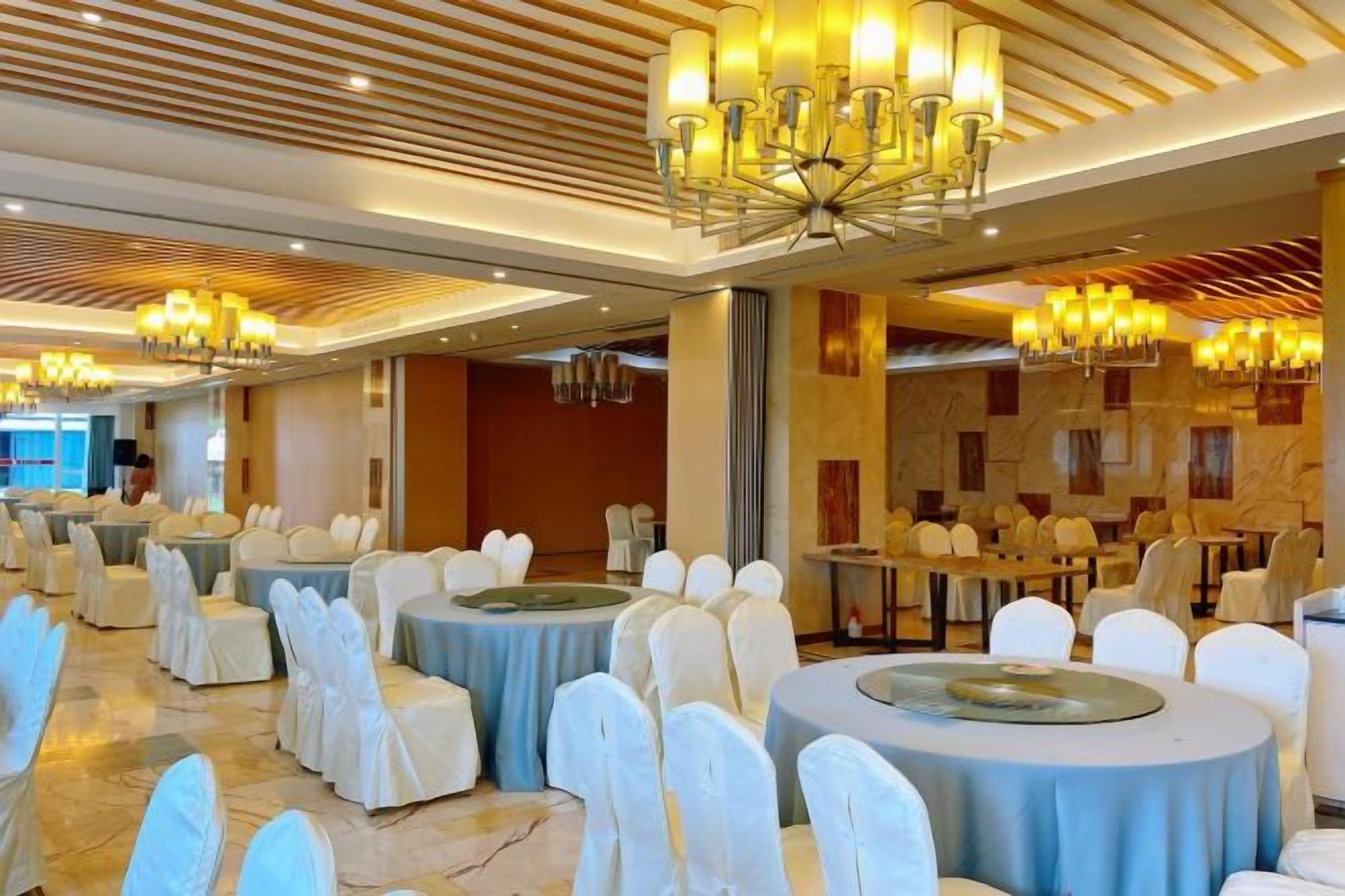 A banquet hall with round tables, white chairs, and chandeliers.