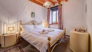 Un dormitorio bien iluminado con techo de madera, cama con ropa blanca, mesita de noche con lámpara y una alfombra decorativa.