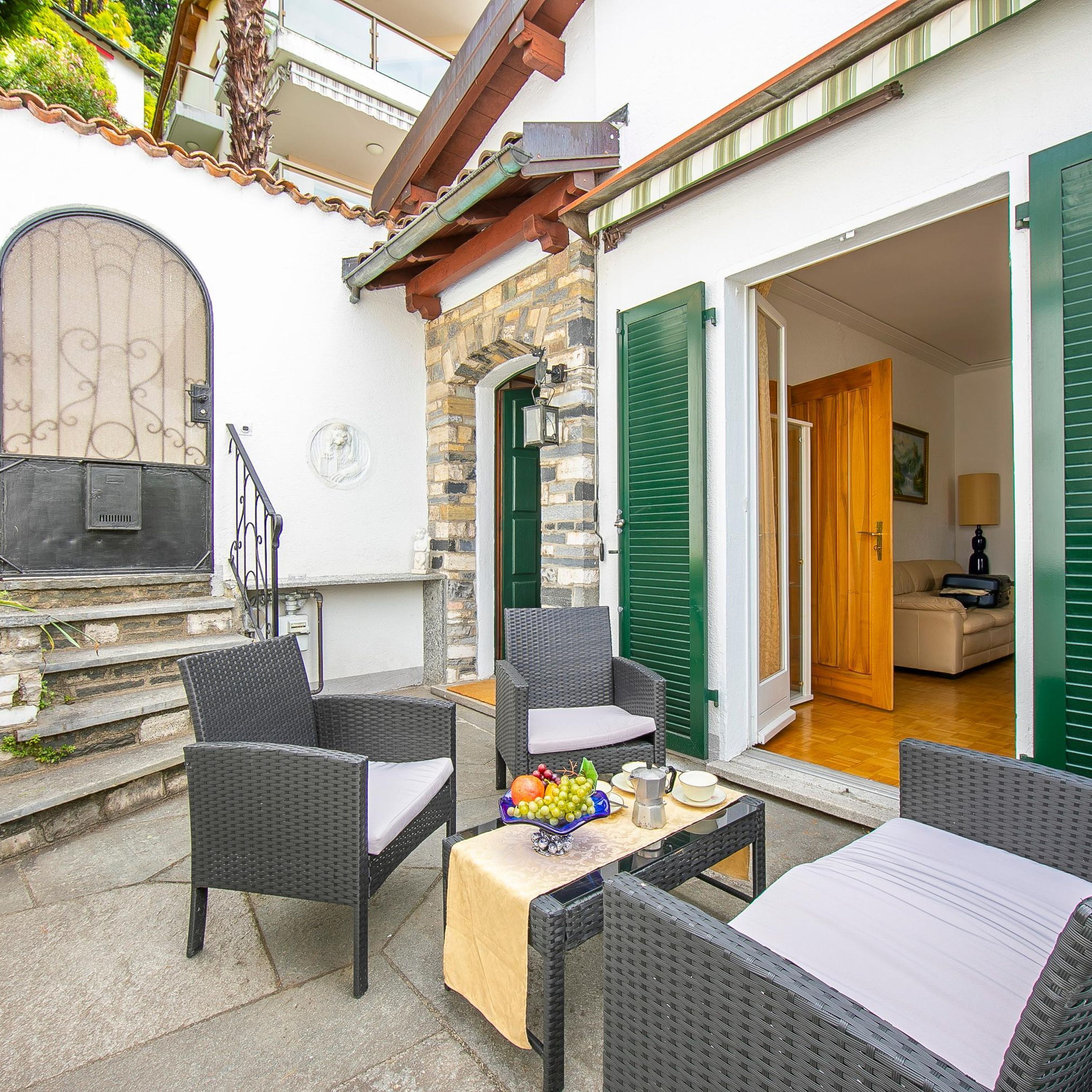 Eine Terrasse mit Korbmöbeln, einem Tisch mit Obst und einer Kaffeekanne sowie einer Steinmauer.