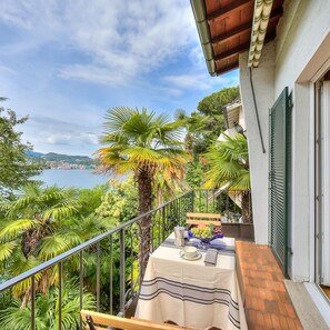 A balcony with a table set for dining, overlooking a scenic view of a body of water and greenery. - Casa Daly in Castagnola Lugano (Lugano)