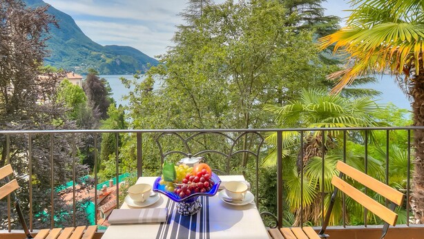 Un balcón con una mesa para dos, con vistas a un paisaje montañoso y una masa de agua.