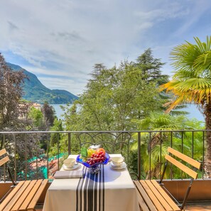 Ein Balkon mit Tisch für Zwei, mit Blick auf eine Berglandschaft und ein Gewässer.