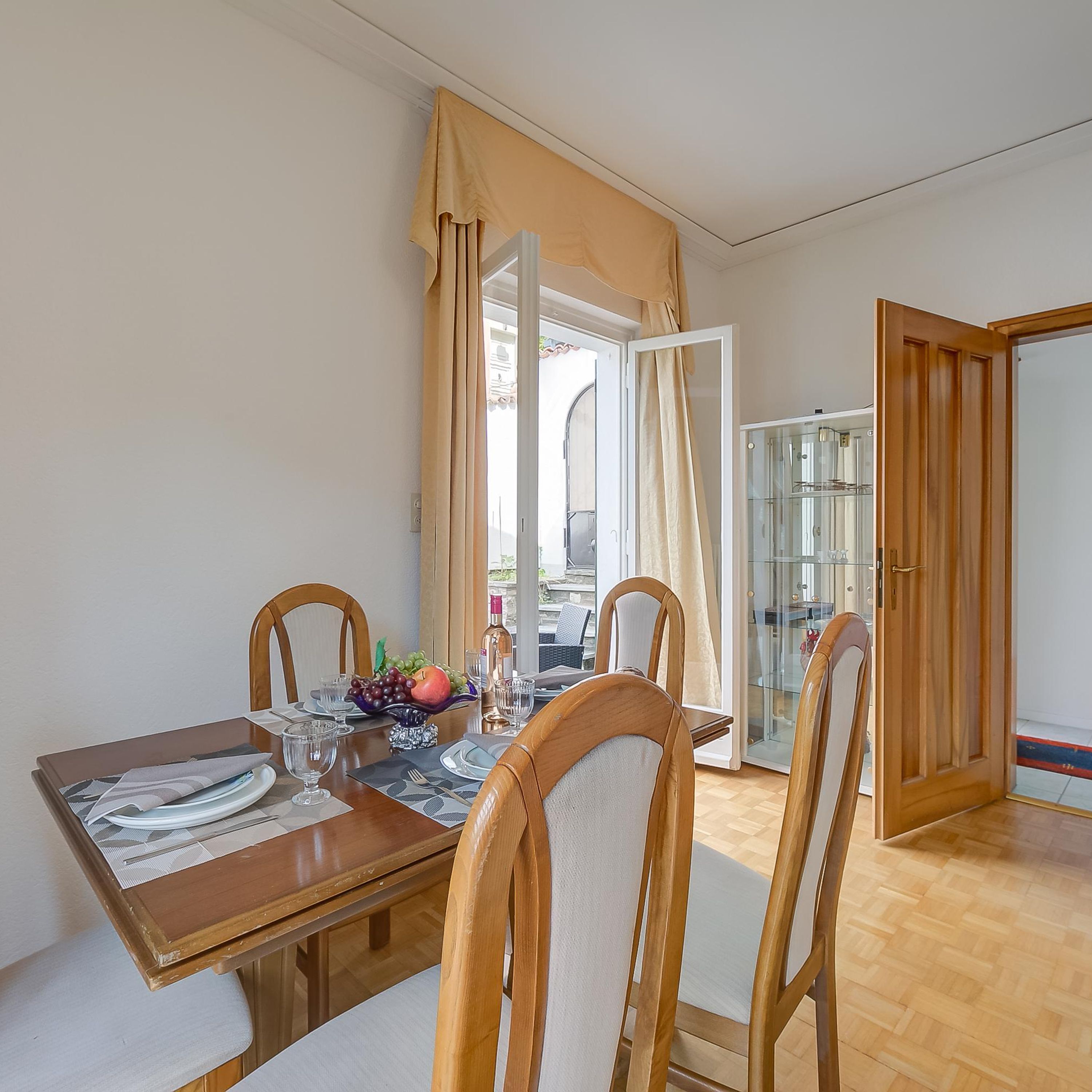 A dining area with a wooden table, four chairs, and a fruit bowl.