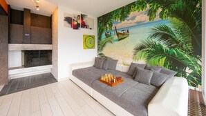 Un soggiorno moderno con un divano grigio, un camino e un murale raffigurante una spiaggia tropicale.