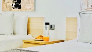 A hotel room with a bed, a bedside table with a croissant and orange juice, and a wall-mounted thermostat.