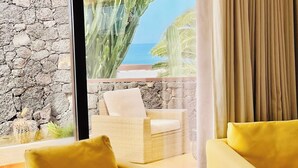 A room with a stone wall, a wicker chair, and a yellow sofa.
