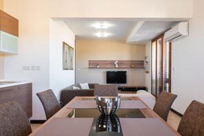A modern dining area with a long table, chairs, a decorative metal centerpiece, a sofa, a flat-screen TV, and a wooden cabinet.