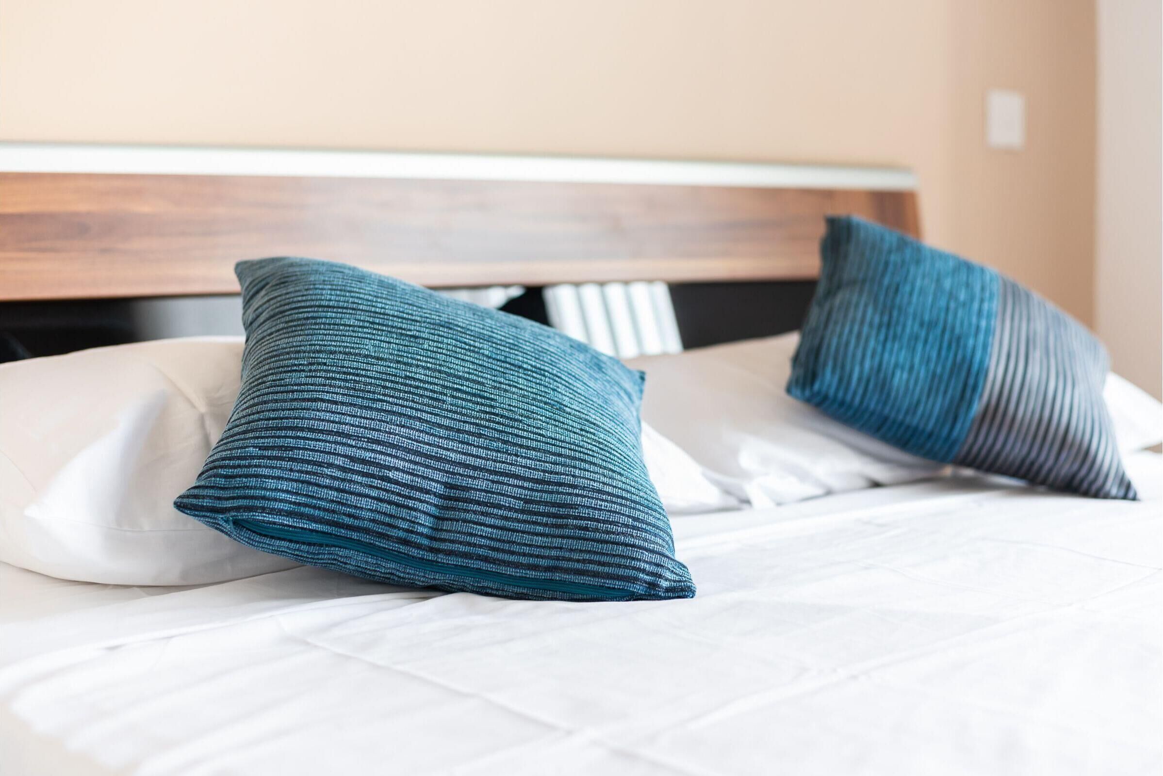 A bed with white bedding and two teal pillows.