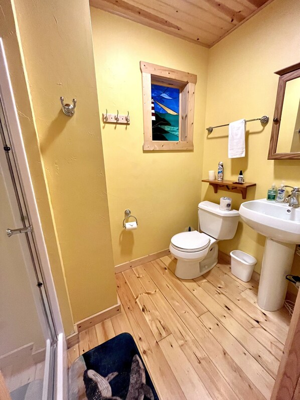 A bathroom with wooden flooring, a toilet, a sink, and a window with a painting.