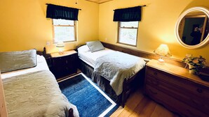Una habitación con dos camas, un ventilador de techo, una ventana con cortinas, un aparador y un espejo.